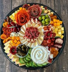 a platter filled with different types of cheeses and fruit on top of a wooden table