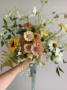 a bouquet of flowers is being held up by someone's hand in front of a white wall