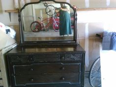 a dresser with a mirror on it and a bicycle in the reflection, behind which is a woman's reflection