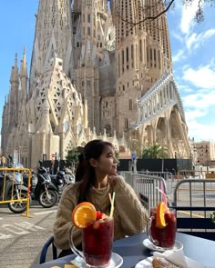 a woman sitting at a table with two drinks in front of a large cathedral like building