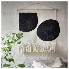 two round black and white wall hangings with tassels on the sides, next to a potted plant