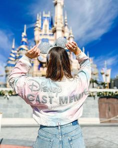 a woman standing in front of a castle wearing a disney world sweatshirt and denim skirt