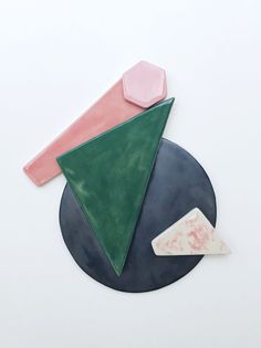 three pieces of art sitting on top of a black plate with pink, green and white shapes