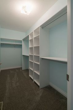 an empty walk in closet with white shelving and carpeted flooring is shown