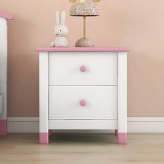 a pink and white nightstand with a gold lamp on it next to a small child's bed