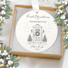 a personalized christmas ornament in a gift box with greenery around it