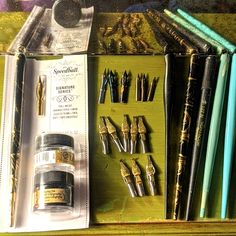 several different types of pens and pencils on a table with other items in the box