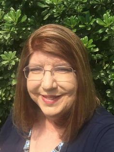 a woman wearing glasses standing in front of bushes