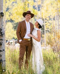 a man and woman standing next to each other in tall grass with trees behind them