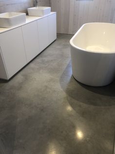 a large white bath tub sitting on top of a cement floor next to two sinks