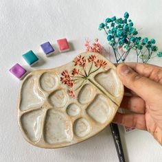 a hand holding a small ceramic object next to some flowers and colored crayons