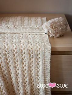 a white knitted blanket sitting on top of a wooden table next to a stuffed animal