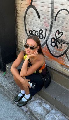 a woman sitting on the ground in front of a graffiti covered wall talking on her cell phone