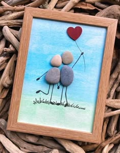 two rocks in the shape of a couple holding a heart shaped balloon on top of some driftwood