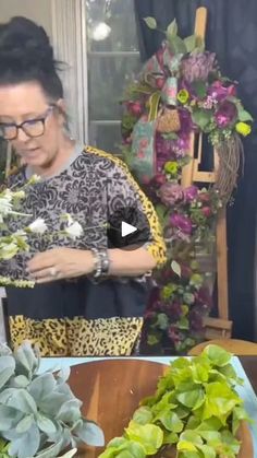 a woman is arranging flowers on a table in front of a window and another plant