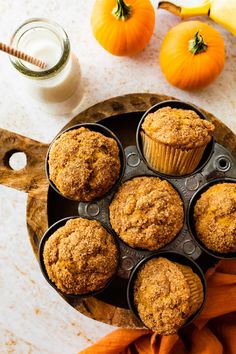 several muffins in a pan on a table next to pumpkins and milk