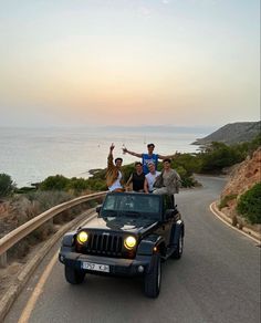 four people are riding in the back of a jeep on a road near the ocean