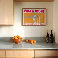 a bowl of oranges sitting on top of a kitchen counter next to bottles of wine