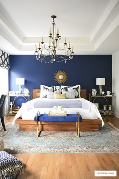 a bedroom with blue walls and white bedding, chandelier above the bed