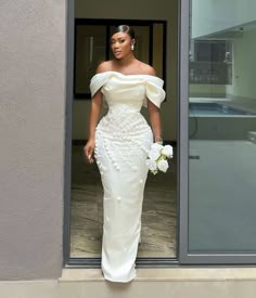 a woman in a white dress standing outside of a building with her hand on her hip