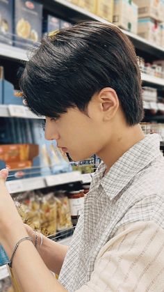 a young man is looking at something in his hand while he shops for food on the shelf