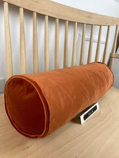 an orange pillow sitting on top of a wooden chair next to a tv remote control