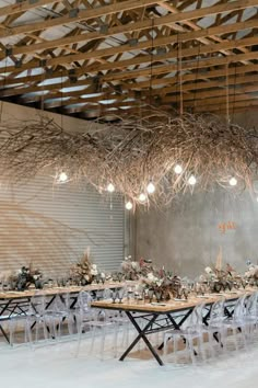 a long table with white chairs and lights hanging from it's ceiling is surrounded by branches