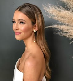 a woman with long hair and earrings standing in front of a black wall wearing a white dress