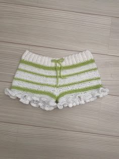 a white and green knitted shorts with ruffles on the bottom sitting on a wood floor