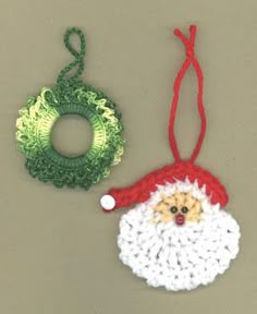 two crocheted christmas ornaments hanging on a gray wall next to a green wreath