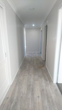 an empty hallway with white walls and wood flooring on the other side, leading to another room