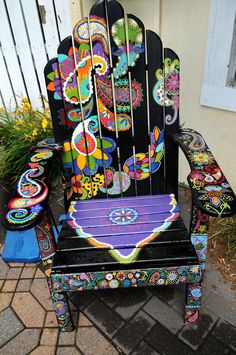 a colorfully painted chair sitting on top of a brick patio next to a white fence