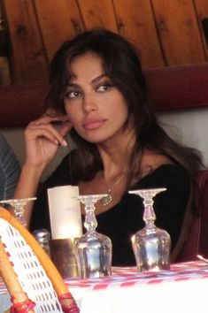 a woman is sitting at a table with wine glasses and candles on the table in front of her