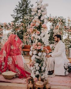 a man and woman sitting next to each other in front of a flower covered structure