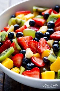 a white bowl filled with fruit salad on top of a wooden table