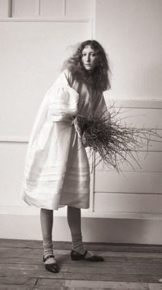 black and white photograph of a woman in dress holding plants with long hair on her head