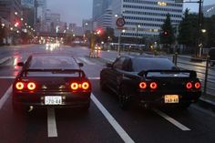 two cars stopped at an intersection in the city with traffic lights on and buildings behind them