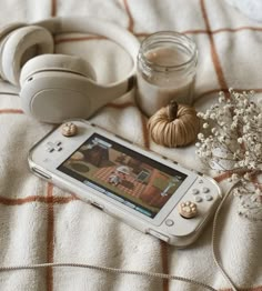 a cell phone sitting on top of a bed next to a vase with flowers and headphones