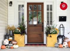 front porch decorated for fall with pumpkins and flowers in planters next to the door