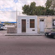 a car is parked in front of a small white building on the side of the road