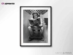 a black and white photo of a man sitting on a toilet reading a book in the bathroom