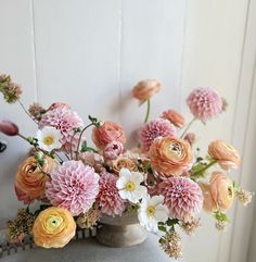 a vase filled with lots of flowers on top of a white table next to a wall