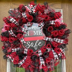 a wreath that says welcome home safe with red and black ribbons hanging on the front door