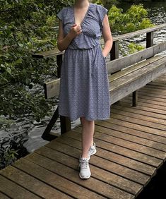 a woman standing on a wooden bridge next to a body of water with trees in the background