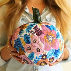 a woman holding a painted pumpkin with flowers on it's front and back sides