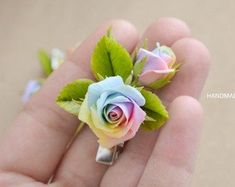 a hand holding a tiny rose ring with green leaves on the outside and pink, blue, yellow and white roses on the inside