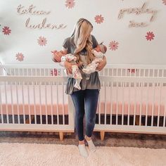 a woman holding two babys in her arms while standing next to a crib