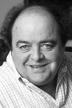 a black and white photo of a man with curly hair smiling at the camera while wearing a button up shirt