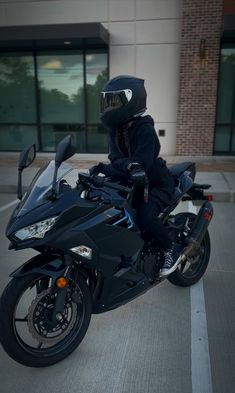 a person riding on the back of a black motorcycle in a parking lot next to a building