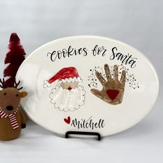 a white plate with two hand prints on it and a reindeer figurine next to it